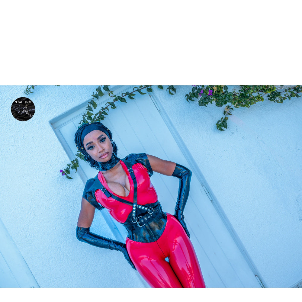 Person wearing a red and black outfit posing against a light blue wall with greenery.