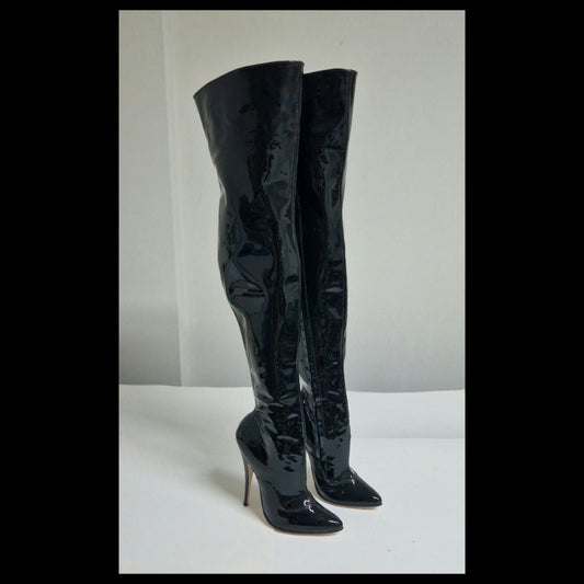 A pair of black patent leather over-the-knee boots with pointed toes and high stiletto heels, standing on a white surface against a white background.