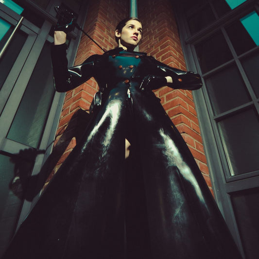 Person in a black superhero costume standing in a dark alley with brick walls.